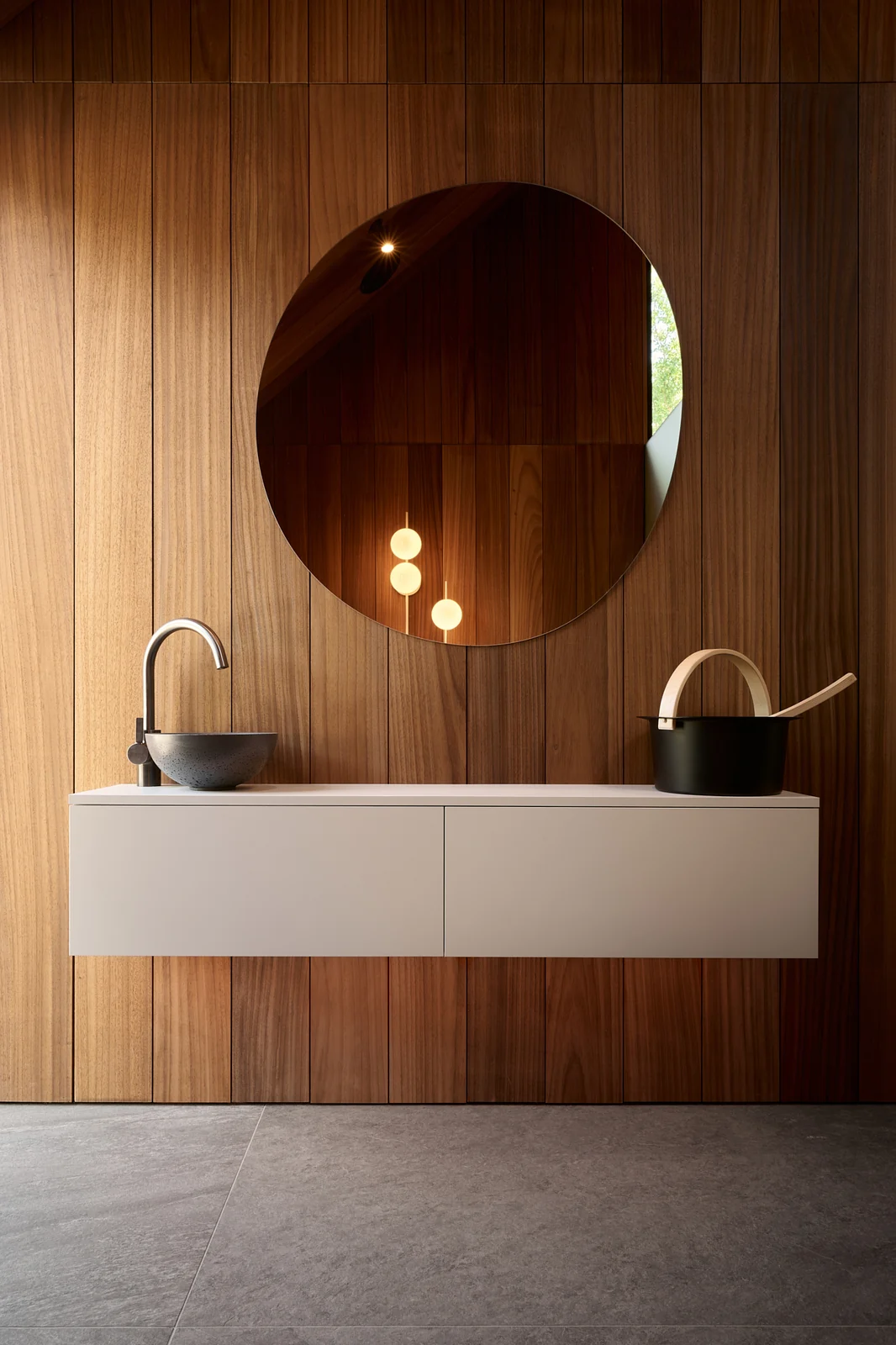 A round mirror and a white cabinet with a stone basin in the sauna house